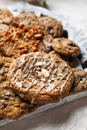 Pile of Chef Crafted Cookies, topped with Earl Grey, Fig Jam and Almond Cookie. Chewy, Gooey, and Crispy cookies topped with sea salt. Definitely the best cookies in San Diego.   These cookies are used for Corporate Catering, Corporate Events, Corporate Gifting, Corporate Orders, and are sourced from the best bakery near me, Magnolia Kitchen and Bakery in La Jolla, San Diego Ca.  Underneath are the best chocolate chip cookies, salted brown butter chocolate chip cookies