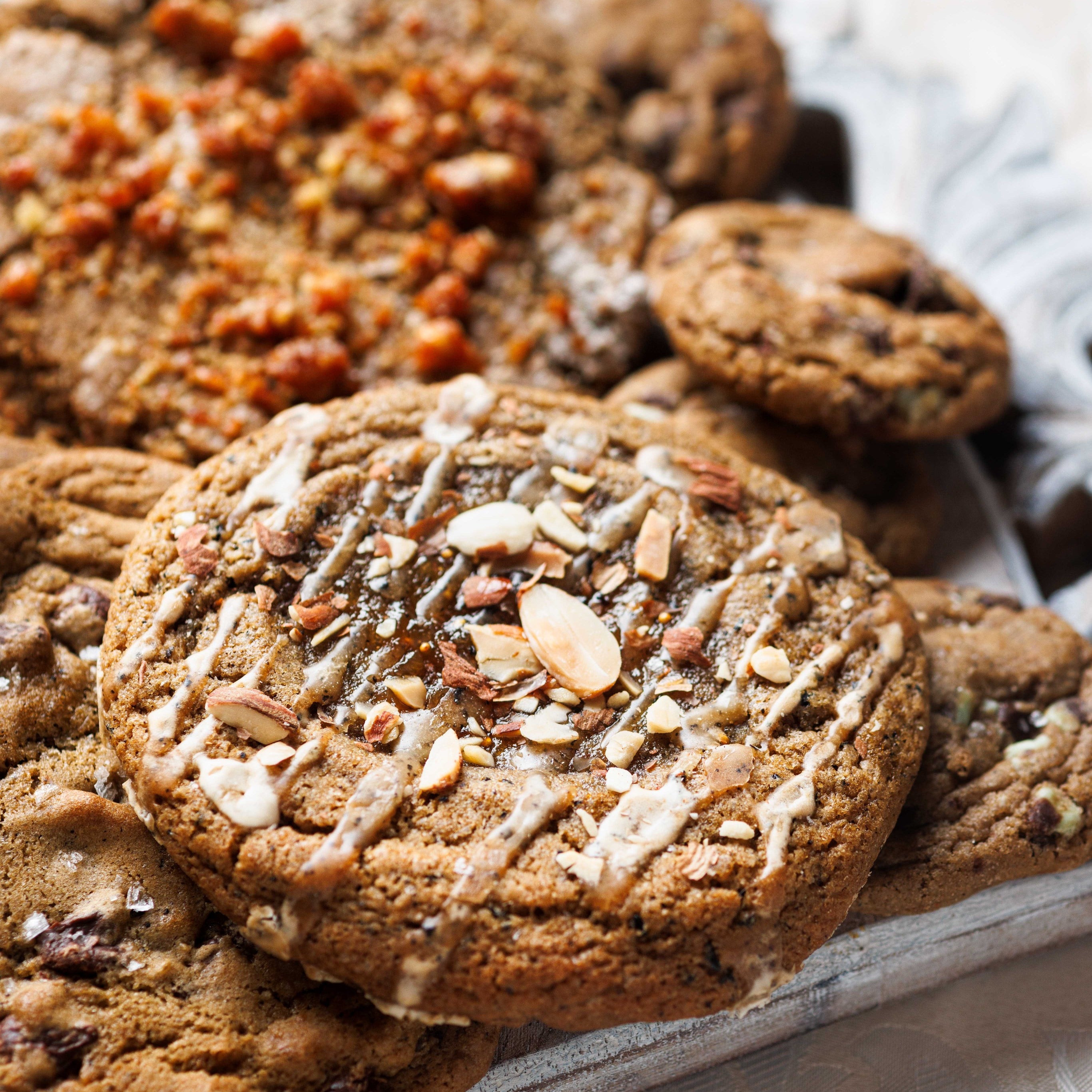 Pile of Chef Crafted Cookies, topped with Earl Grey, Fig Jam and Almond Cookie. Chewy, Gooey, and Crispy cookies topped with sea salt. Definitely the best cookies in San Diego.   These cookies are used for Corporate Catering, Corporate Events, Corporate Gifting, Corporate Orders, and are sourced from the best bakery near me, Magnolia Kitchen and Bakery in La Jolla, San Diego Ca.  Underneath are the best chocolate chip cookies, salted brown butter chocolate chip cookies