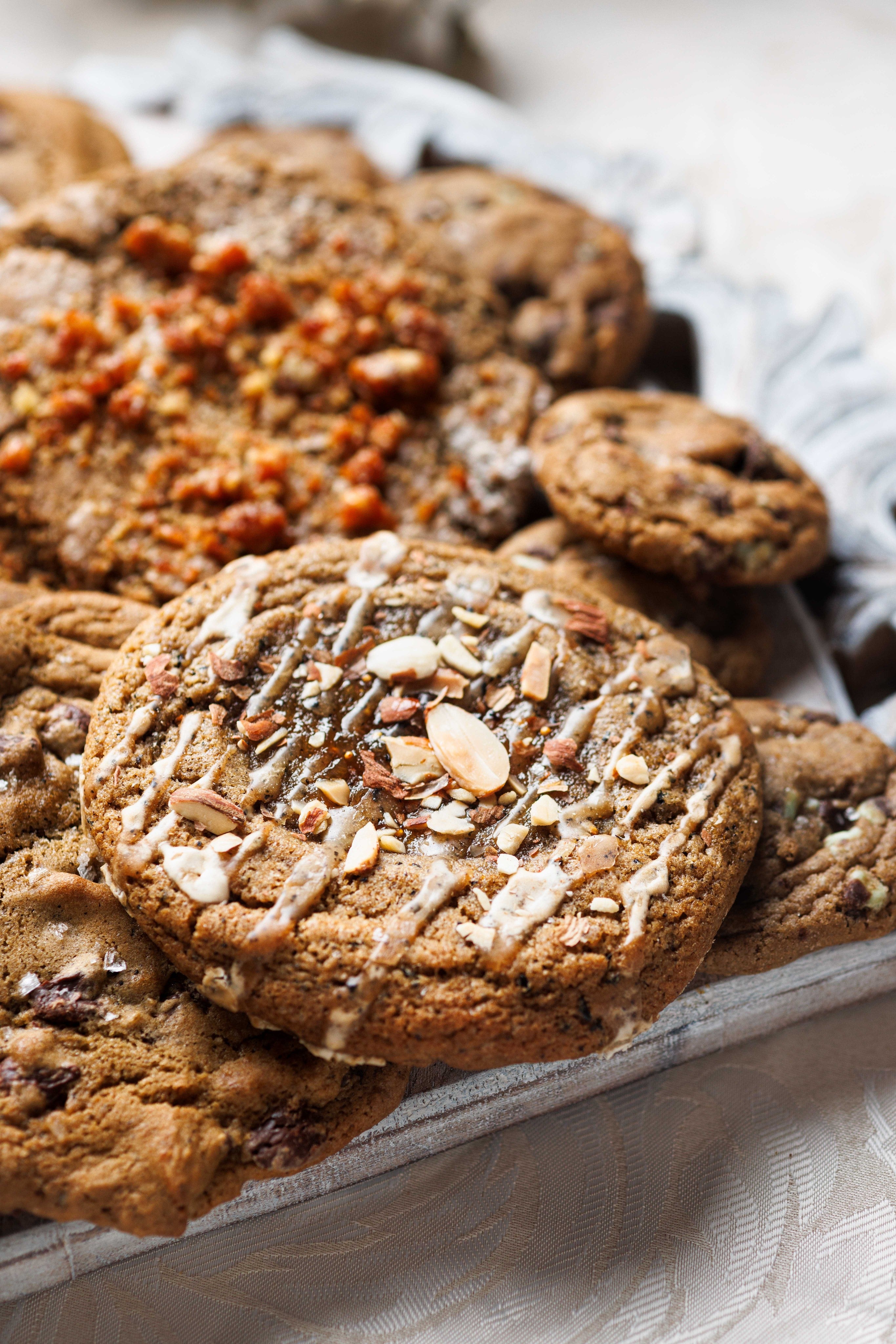 Pile of Chef Crafted Cookies, topped with Earl Grey, Fig Jam and Almond Cookie. Chewy, Gooey, and Crispy cookies topped with sea salt. Definitely the best cookies in San Diego.   These cookies are used for Corporate Catering, Corporate Events, Corporate Gifting, Corporate Orders, and are sourced from the best bakery near me, Magnolia Kitchen and Bakery in La Jolla, San Diego Ca.  Underneath are the best chocolate chip cookies, salted brown butter chocolate chip cookies