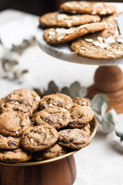 Cake Stand full of Mint Chocolate Chip Cookies with Andes Mints speckled throughout.  A cake stand of Earl Grey Cookies in the background shingled on eachother with Almonds and Fig jam.  The cookies are gooey, soft and chewy, and full of chocolatey goodness. The Andes Mint Chocolate Chip Cookies are perfectly baked, with crinkly tops and sea salt sprinkled all over.  Best Chocolate Chip Cookies, absolutely delicious and the best chocolate chip cookie recipe ever. 